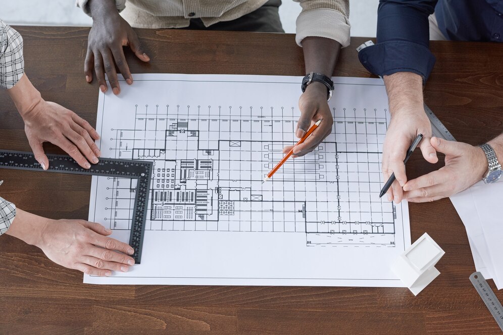high-angle-view-engineers-drawing-with-pencil-measuring-with-ruler-they-working-blueprint-table_249974-8541